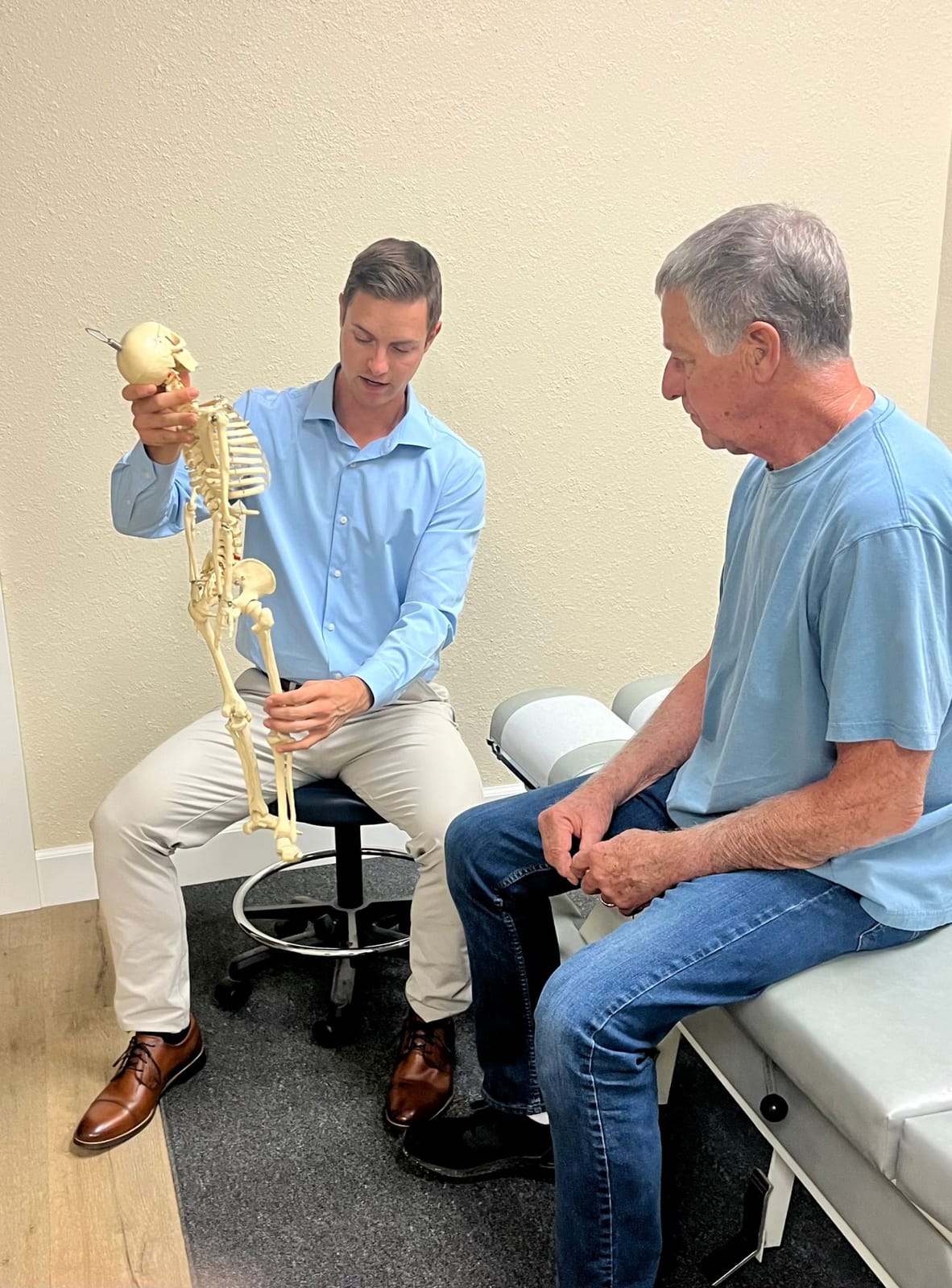 Dr. Hill using a skeleton model to explain the spine to a patient seated on the treatment table